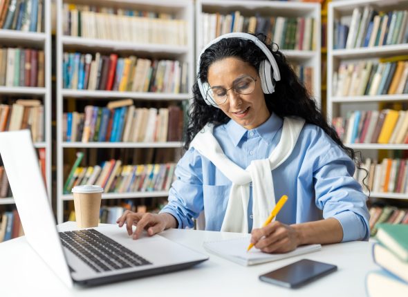 Focused woman studying at library desk with laptop and headphones